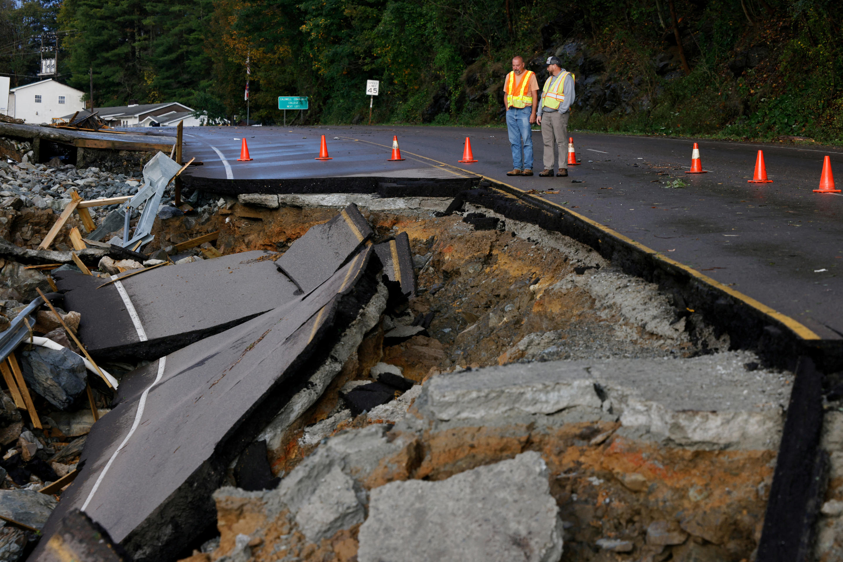 Workers standing near emergency cones examine a large section of Highway 105 washed away by flooding during Tropical Storm Helene.