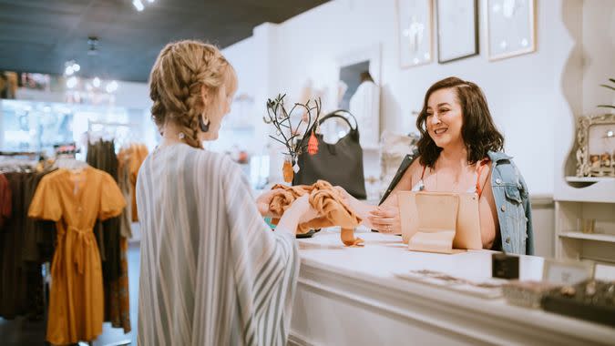 A fashionable Hispanic woman works in her small retail clothing store, selling new fashion items.