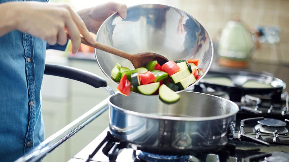 Midsection of woman adding fresh chopped vegetables in saucepan.