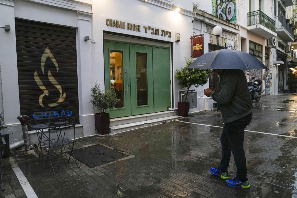A man holding an umbrella stands in front of a Jewish restaurant that Greek officials believe was one of the targets of a planned terrorist attack, in central Athens, Tuesday, March 28, 2023. Greek police said Tuesday they have arrested two terrorism suspects with Pakistani origin, who had been planning attacks in the country aimed at causing mass casualties. (AP Photo/Thanassis Stavrakis)