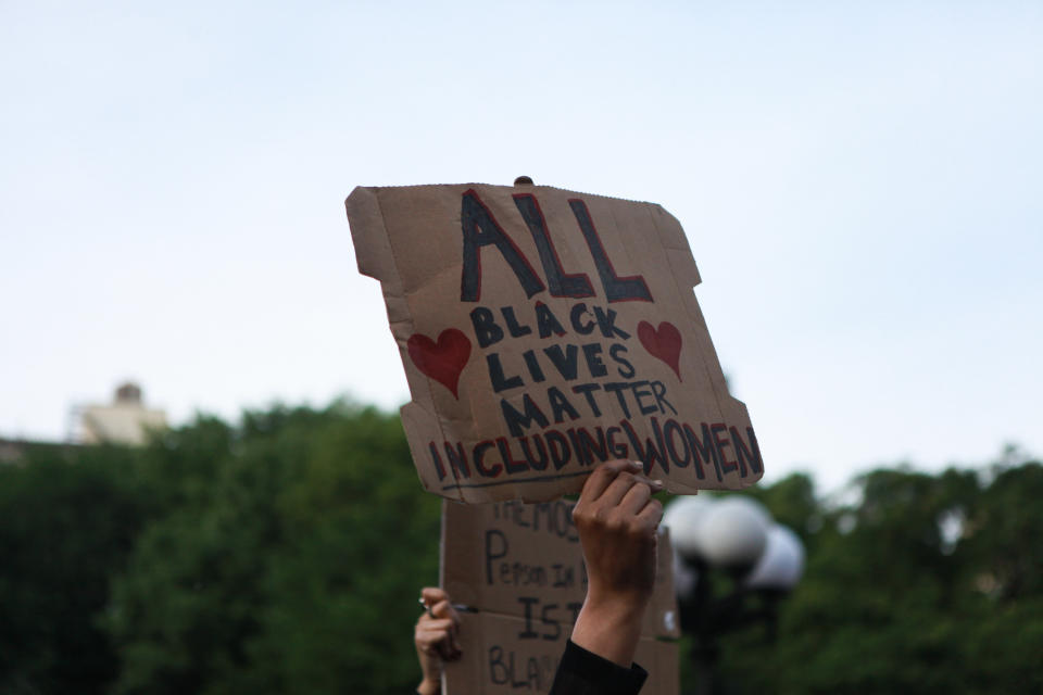 An activist holding up a sign that reads, "All black lives matter, including women."