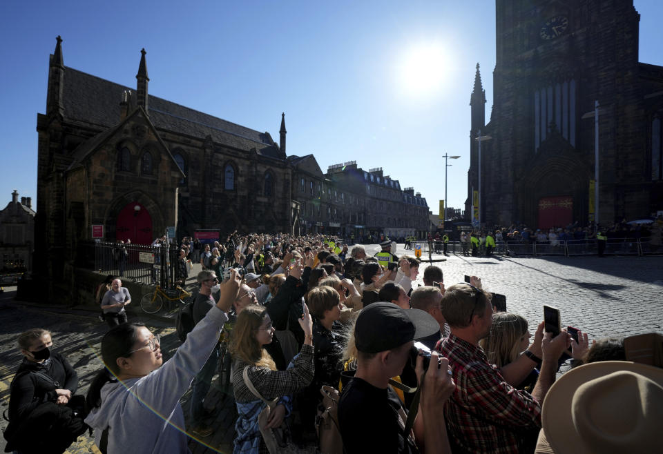 People take photos with their mobile phones along route prior to the departure of the hearse carrying Queen Elizabeth's coffin from St Giles Cathedral to Edinburgh Airport in Edinburgh, Scotland, Tuesday, Sept. 13, 2022. After lying in the cathedral most of Tuesday, the queen's coffin will be flown back to London and driven to her official London home, Buckingham Palace. (AP Photo/Jon Super)