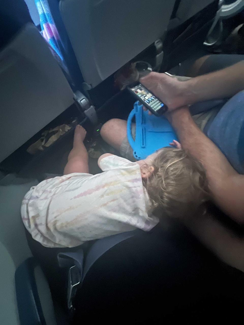 A baby laying across the laps of its parents on the airplane.