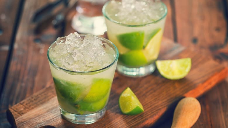 Two Caipirinha cocktails with lime wedges