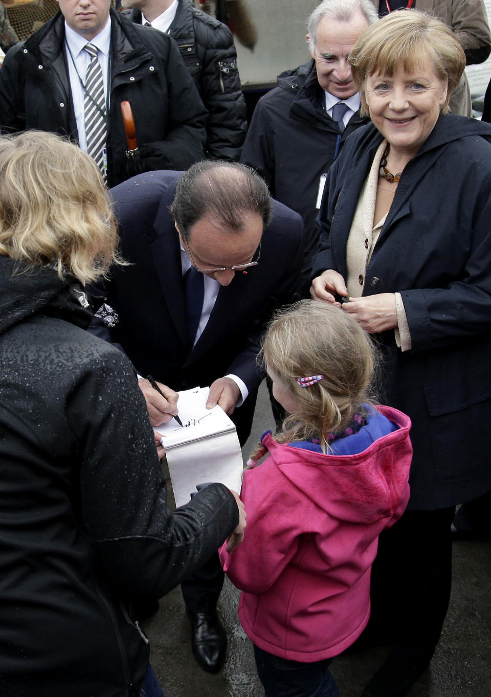 German Chancellor Angela Merkel, right, smiles as President of France Francois Hollande, center, gives an autograph to 6 years old tourist Hanna during a visit of the Baltic see island Ruegen, northern Germany, Friday, May 9, 2014. Merkel and Hollande meet for two days on the island Ruegen and in the coastal city of Stralsund. (AP Photo/Michael Sohn)