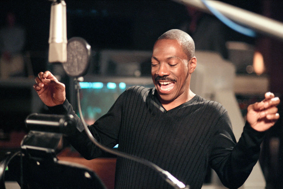 Eddie Murphy, wearing a sweater, energetically performs at a recording studio