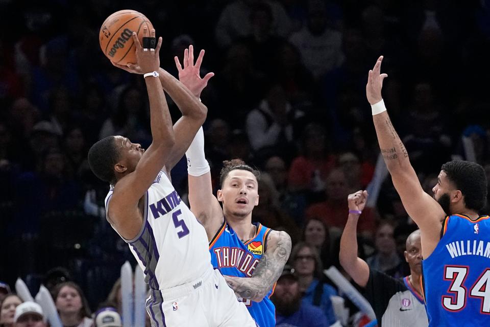 Sacramento Kings guard De'Aaron Fox (5) shoots in front of Oklahoma City Thunder forward Lindy Waters III, center, and forward Kenrich Williams (34) in the second half of an NBA basketball game Sunday, Feb. 26, 2023, in Oklahoma City. (AP Photo/Sue Ogrocki)