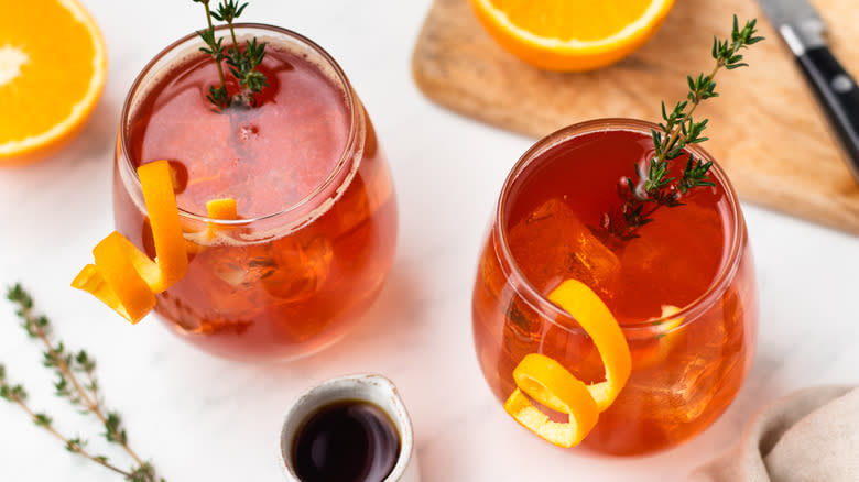 Two cranberry cocktails with orange and thyme garnishes