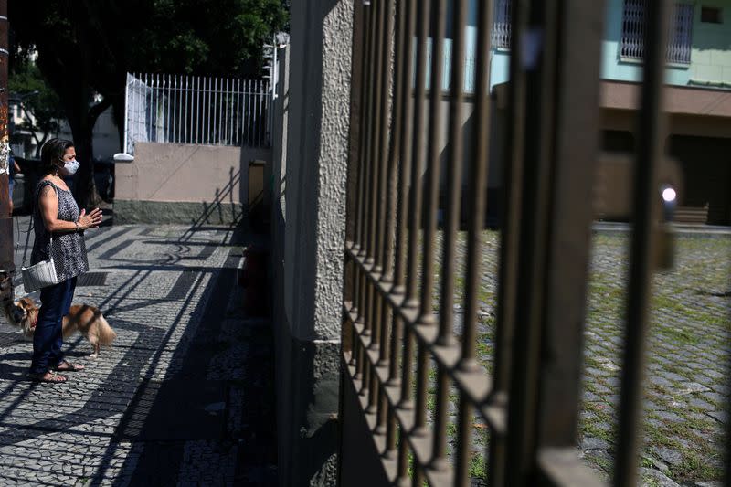 A woman wearing a protective face mask prays outside a church as priest Jorge Luiz de Oliveira delivers the Angelus prayer from the balcony of the Santuario Basilica de Sao Sebastiao, following the coronavirus disease (COVID-19) outbreak, in Rio de Janeiro