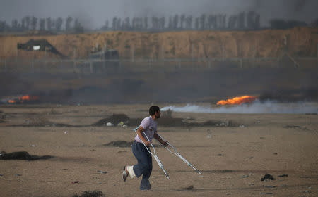 A demonstrator with crutches runs for cover during a protest where Palestinians demand the right to return to their homeland, at the Israel-Gaza border in the southern Gaza Strip May 25, 2018. REUTERS/Ibraheem Abu Mustafa