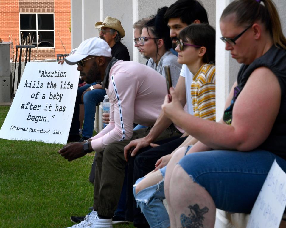 Attendees on both sides of the abortion debate sit in the shade of Abilene City Hall during Saturday's Abilene "Bans off our Bodies" Rally. While at least 80 came to demonstrate for abortion rights, about six anti-abortion activists were also seen quietly attending with their own signs.