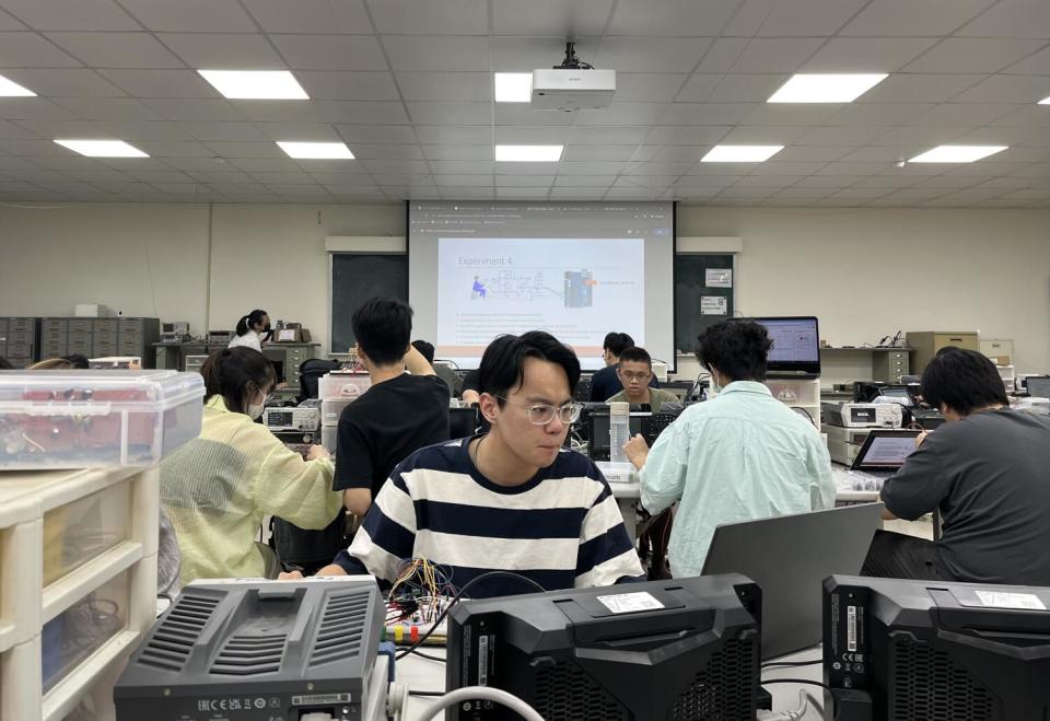 A student working at a laptop with fellow students and a projector screen behind him