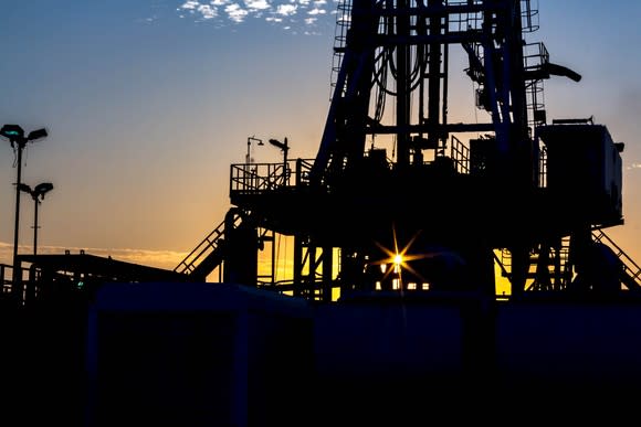 A drilling rig with the sun setting in the background.