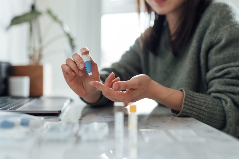 cropped shot of young woman using blood test kit at home