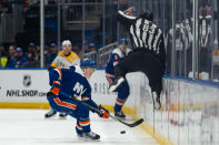 Linesman Matt MacPherson (83) jumps to avoid a puck played toward New York Islanders' Simon Holmstrom, left, during the first period of the Islanders' NHL hockey game against the Nashville Predators in Elmont, N.Y., Saturday, April 6, 2024. (AP Photo/Peter K. Afriyie)