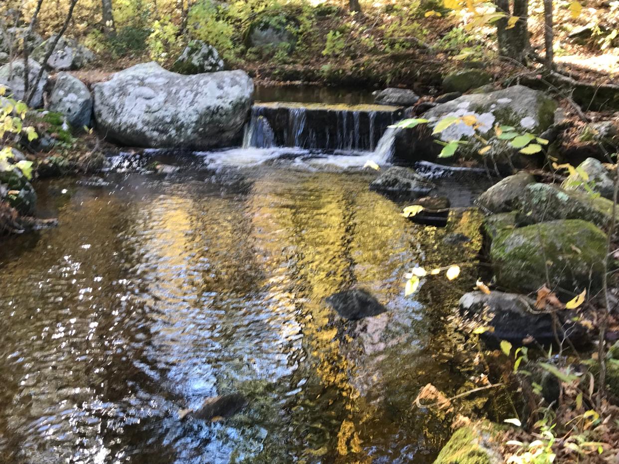 A small waterfall tumbles over a rectangular granite block placed in a stream that flows to Breakheart Pond.