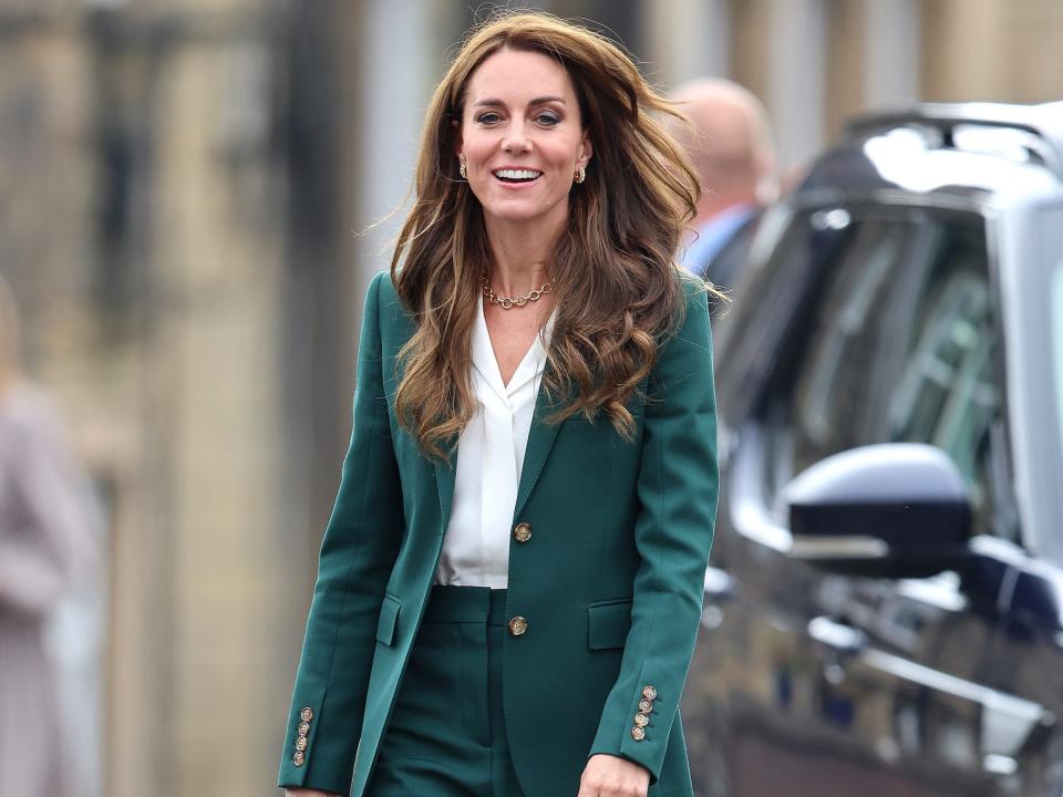 Kate Middleton walks in a green suit next to a car.