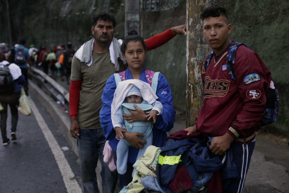 In this Oct. 18, 2018 photo, Honduran migrants David Cruz, 18, right, his wife Scarlet Romero, 16, holding their 3-month-old son David Ezequiel, pose for a photo, accompanied by another migrant as they leave Guatemala City with a caravan of thousands. Scarlet and David say the left a home where they were harassed by gangs and were without job opportunities. Romero said she left behind a 2-year-old daughter with her grandmother. (AP Photo/Moises Castillo)