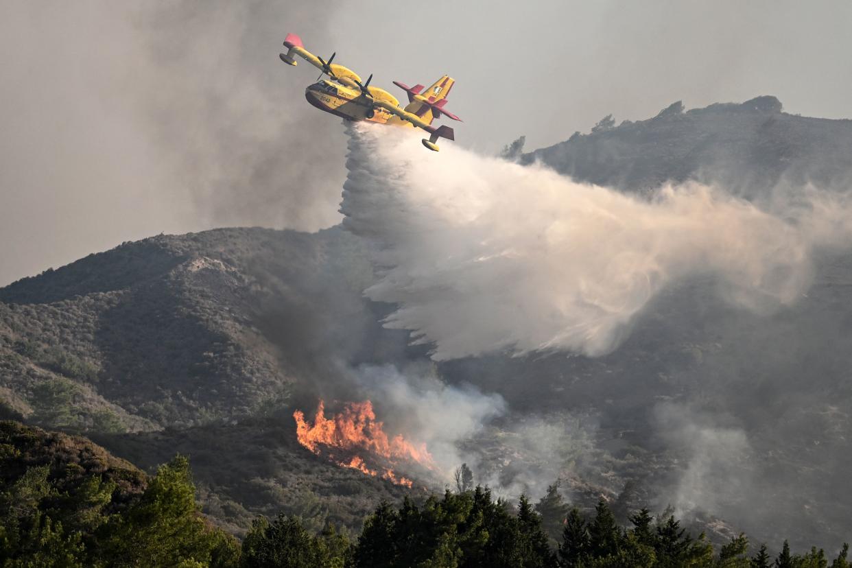 A fire fighting aircraft drops water over a wildfire close to village of Vati  in the southern part of the Greek island of Rhodes, about 70 km southwest of the capital city on July 25, 2023. Some 30,000 people fled the flames on Rhodes at the weekend, the country's largest-ever wildfire evacuation as the prime minister warned that the heat-battered nation was 