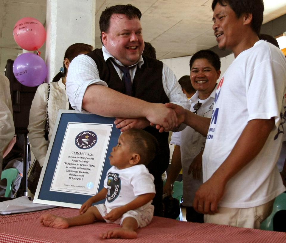 Craig Glenday, then a Guinness World Records adjudicator, congratulates Reynaldo Balawing, father of Junrey Balawing, sitting on the table, after presenting him with a Guinness World Record certificate.