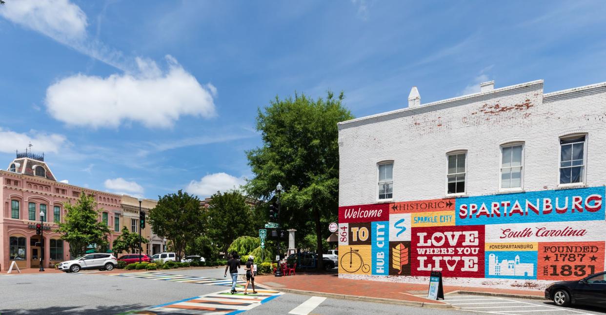 Spartanburg, SC, USA-13 June 2021: The heart of downtown, showing painted building welcome sign, Victorian building on the left of Boulevard, and a young couple walking.  Horizontal image.