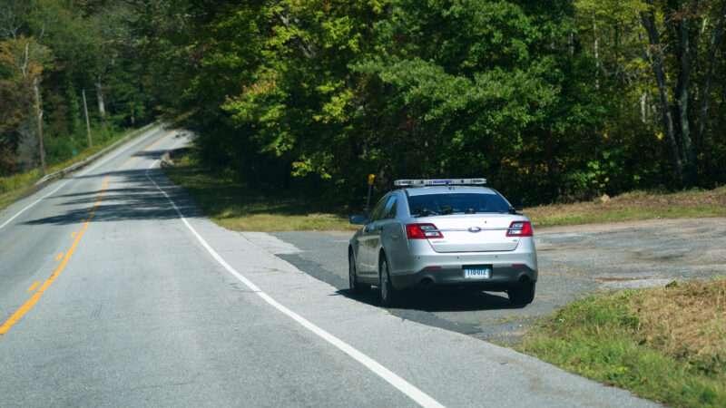 A Connecticut State Patrol car sits along the side of a two-lane highway.