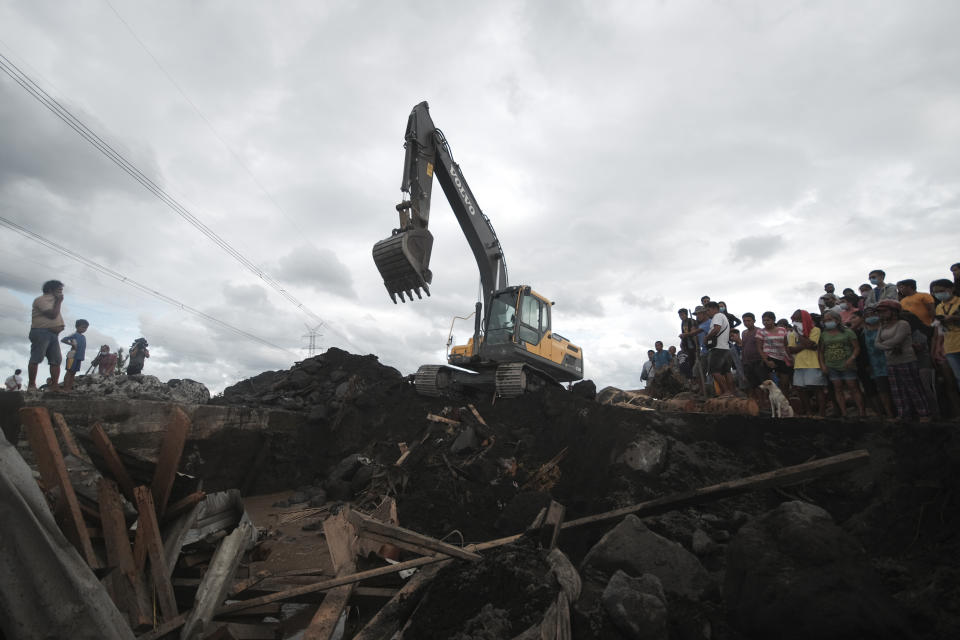Residents watch as a backhoe clears boulders and mudflows from Mayon Volcano triggered by heavy rains from Typhoon Goni in the town of Guinobatan, Albay province, central Philippines on Monday, Nov. 2, 2020. More than a dozen of people were killed as Typhoon Goni lashed the Philippines over the weekend, and about 13,000 shanties and houses were damaged or swept away in the eastern island province that was first hit by the ferocious storm, officials said Monday. (AP Photo/John Michael Magdasoc)