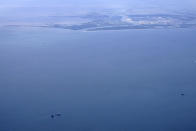 The capsized lift boat Seacor Power and two rescue boats, bottom left, are seen seven miles off the coast of Louisiana in the Gulf of Mexico Sunday, April 18, 2021. The vessel capsized during a storm on Tuesday. Port Fourchon and Bayou Lafourche, where the ship left port, are seen above. (AP Photo/Gerald Herbert)