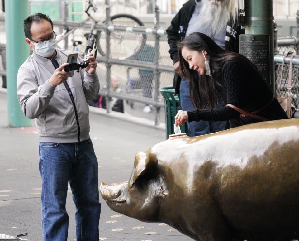 Tourists in face masks take pictures of a pig statue at the Pike Place Market in Seattle on March 5, 2020, during an outbreak of coronavirus that prompted local authorities to recommend that people temporarily work from home and avoid large gatherings.