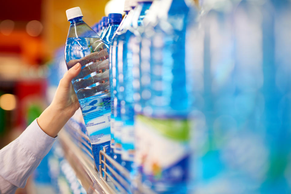 Pictured is a female hand taking bottle of mineral water from supermarket shelf.