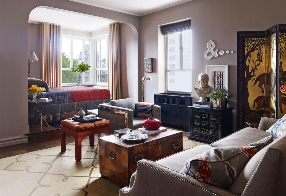 a living room with a rounded arch and built in bed by the window and linen sofa with studs and a black and yellow oriental screen and other furniture