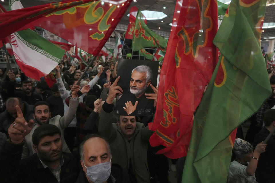 Mourners wave Iranian and Islamic flags during a ceremony marking anniversary of the death of the late Revolutionary Guard Gen. Qassem Soleimani, shown in the poster, who was killed in Iraq in a U.S. drone attack in 2020, at Imam Khomeini Grand Mosque in Tehran, Iran, Tuesday, Jan. 3, 2023. Iran's President Ebrahim Raisi on Tuesday vowed to avenge the killing of the country's top general on the third anniversary of his death, as the government rallied its supporters in mourning amid months of anti-government protests. (AP Photo/Vahid Salemi)