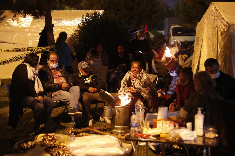 Local residents living in tents outdoors try to stay warm in Izmir, Turkey, Monday, Nov. 2, 2020. In scenes that captured Turkey's emotional roller-coaster after a deadly earthquake, rescue workers dug two girls out alive Monday from the rubble of collapsed apartment buildings three days after the region was jolted by quake that killed scores of people. Close to a thousand people were injured. (AP Photo/Darko Bandic)