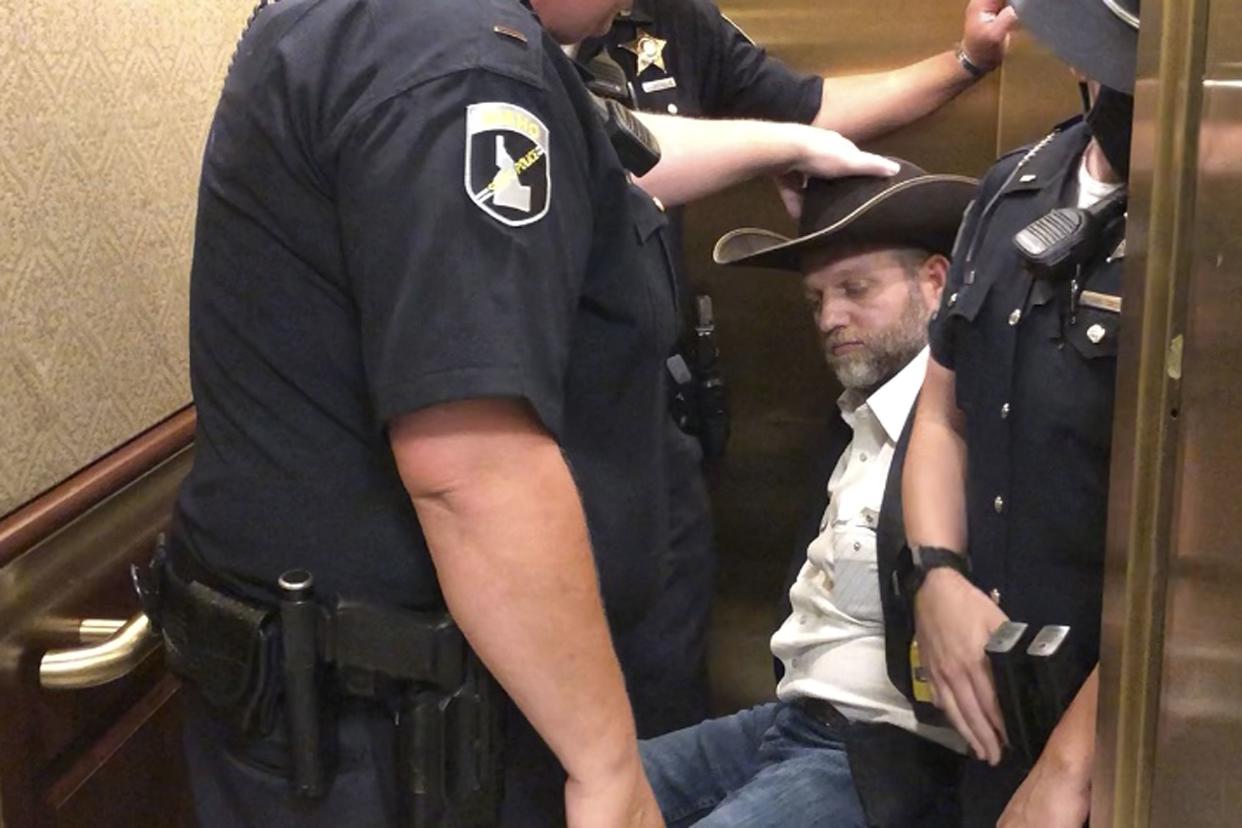 This image taken from video shows anti-government activist Ammon Bundy, rear, being wheeled into an elevator in a chair following his arrest at the Idaho Statehouse in Boise, Idaho, Tuesday, Aug. 25, 2020. 