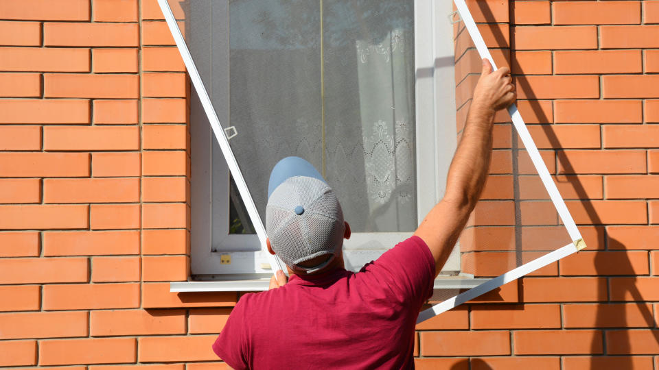 Someone fitting window screens to repel insects