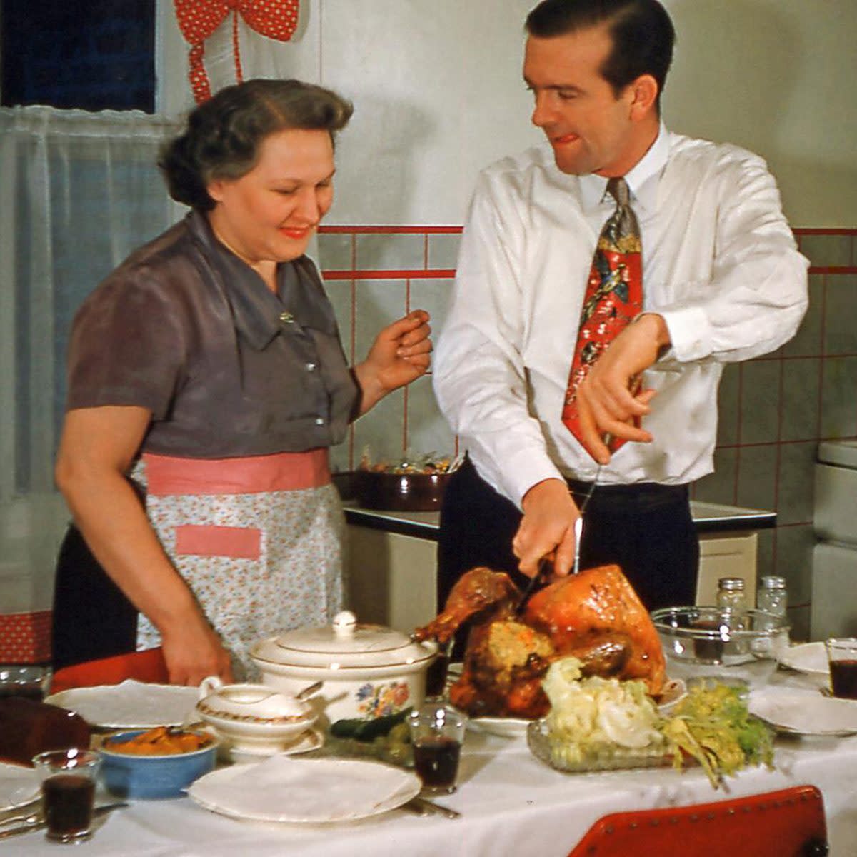 Husband carves the turkey with a silly face while wife watches on