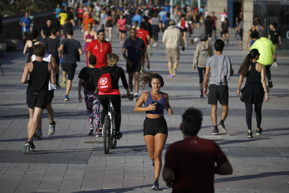 People exercise on a seafront promenade in this photo taken with a telephoto lens in Barcelona, Spain, Saturday, May 2, 2020. Spaniards have filled the streets of the country to do exercise for the first time after seven weeks of confinement in their homes to fight the coronavirus pandemic. People ran, walked, or rode bicycles under a brilliant sunny sky in Barcelona on Saturday, where many flocked to the maritime promenade to get as close as possible to the still off-limits beach. (AP Photo/Emilio Morenatti)