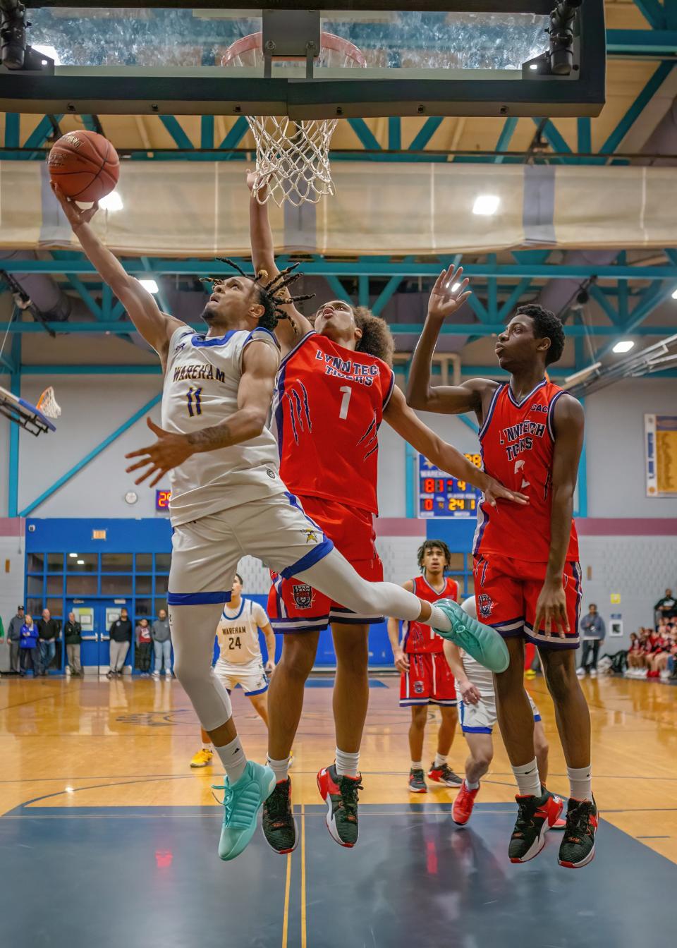 Jakwon Pittman (11) of Wareham High lays the ball up underneath the basket as Lynn Voc-Tech forward Jayden Welch (1) attempts to block the shot.