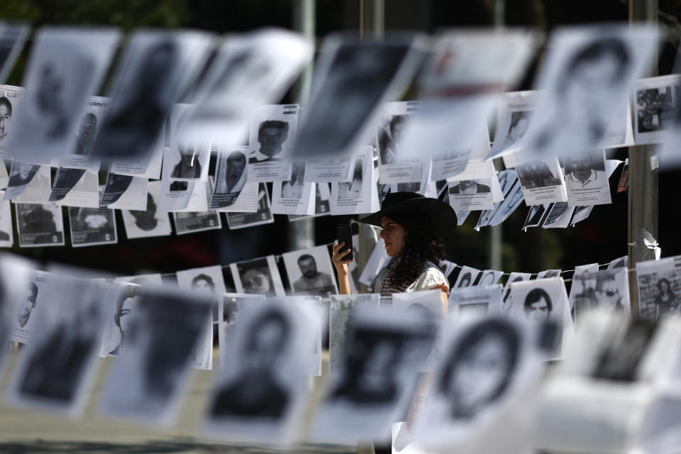 Framed by images of people who have been disappeared, a woman takes photos during a Mother's Day march in Mexico City, Friday, May 10, 2019. Mothers and other relatives of persons gone missing in the fight against drug cartels and organized crime are demanding that authorities locate their loved ones. (AP Photo/Eduardo Verdugo)