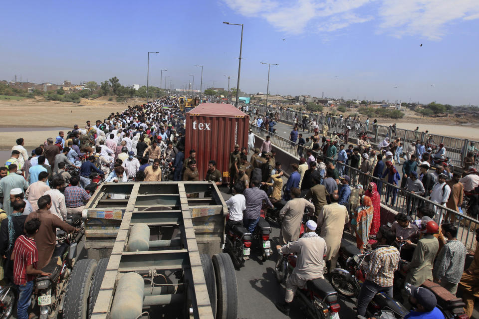 People cross a bridge on Ravi River which is closed for traffic due to shipping containers placed by authorities in an attempt to foil a planned protest, in Lahore, Pakistan, Tuesday, May 24, 2022. Pakistan's key opposition party led by recently ousted Prime Minister Imran Khan accused police of detaining hundreds of its supporters in raids that started early Tuesday. (AP Photo/K.M. Chaudary)