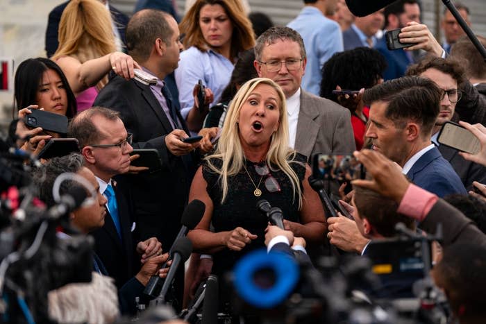 Marjorie Taylor Greene, surrounded by reporters and cameras, speaks passionately at a crowded press event