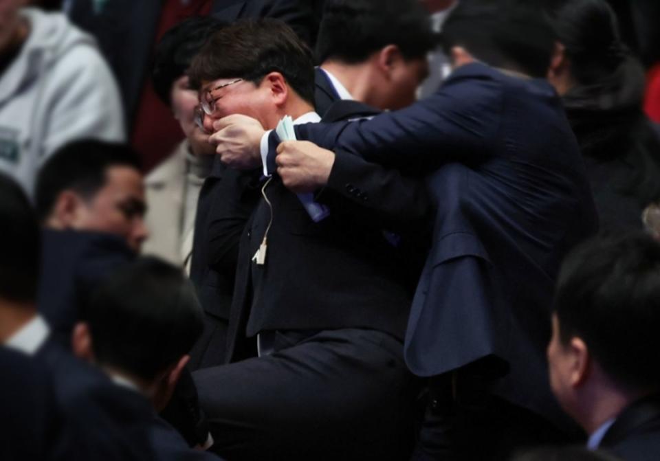 在野黨議員姜聖熙因跟總統尹錫悅多說兩句話，遭維安人員摀嘴架離現場。（翻攝自推特@kangjinbo）