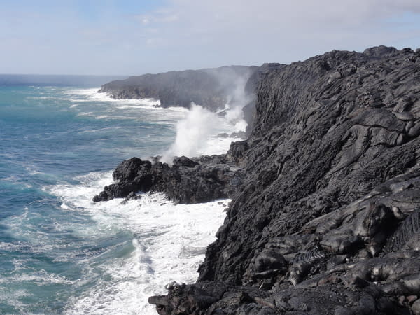 Lava from Kilauea volcano in Hawaii drops into the ocean. Steam plumes rise where the hot molten rock meets the sea.