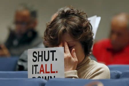 A woman presses her forehead as she sits with a group of Porter Ranch residents holding protest signs at a meeting of air quality regulators to discuss potential rules against the utility that operates the site of a gas leak in Porter Ranch, in Diamond Bar, California, United States, January 20, 2016. REUTERS/Lucy Nicholson