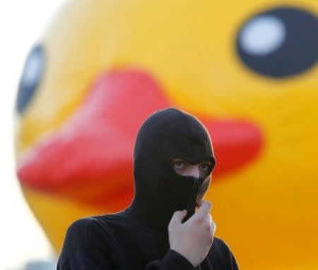 A masked man is pictured in front of a rubber duck, which is the symbol of protest against the Belgrade Waterfront project in Belgrade, Serbia, June 25, 2016. REUTERS/Djordje Kojadinovic