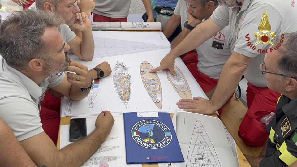 In this photo released by Italian Firefighters on Tuesday, August 20, 2024, scuba divers examine a map of the sailing yacht Bayesian in the port of Porticello. Rescuers and divers returned to the site of a superyacht that sank in a storm on Tuesday and began searching for six people, including British tech mogul Mike Lynch, who are thought to still be trapped in the hull 50 meters (164 feet) under water. (AP, HO via Italian Firefighters)