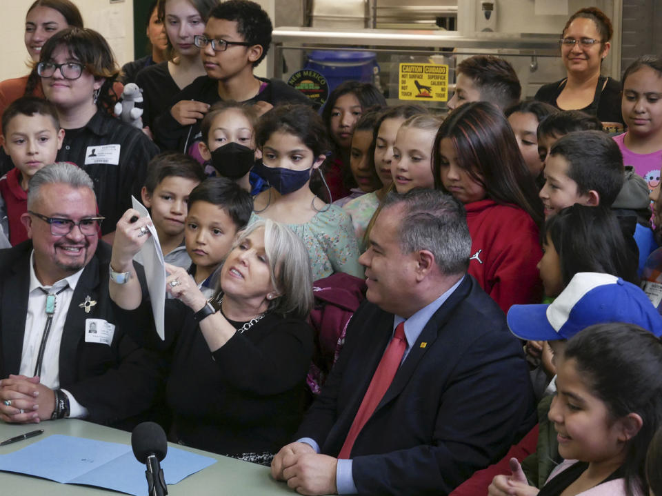 New Mexico Gov. Michelle Lujan Grisham, center, holds up a bill she signed that provides free school meals to all students regardless of their family incomes during a ceremony at an elementary school in Santa Fe, N.M., Monday, March 27, 2023. (Matt Dahlseid/Santa Fe New Mexican via AP)