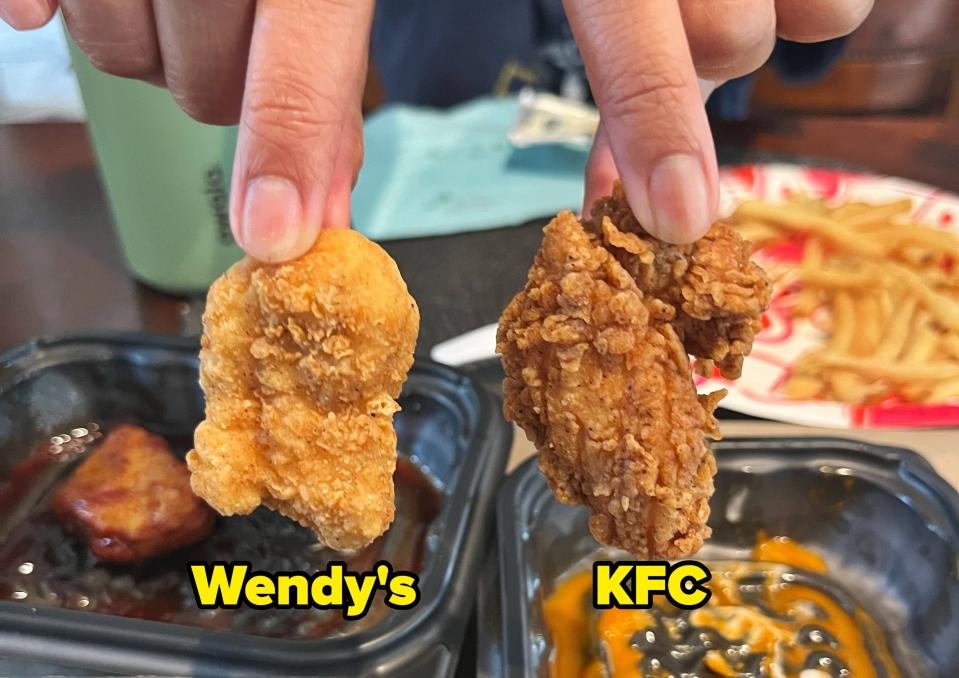 Person holding a chicken nugget and a fried chicken piece above dipping sauces, served with fries in a food container