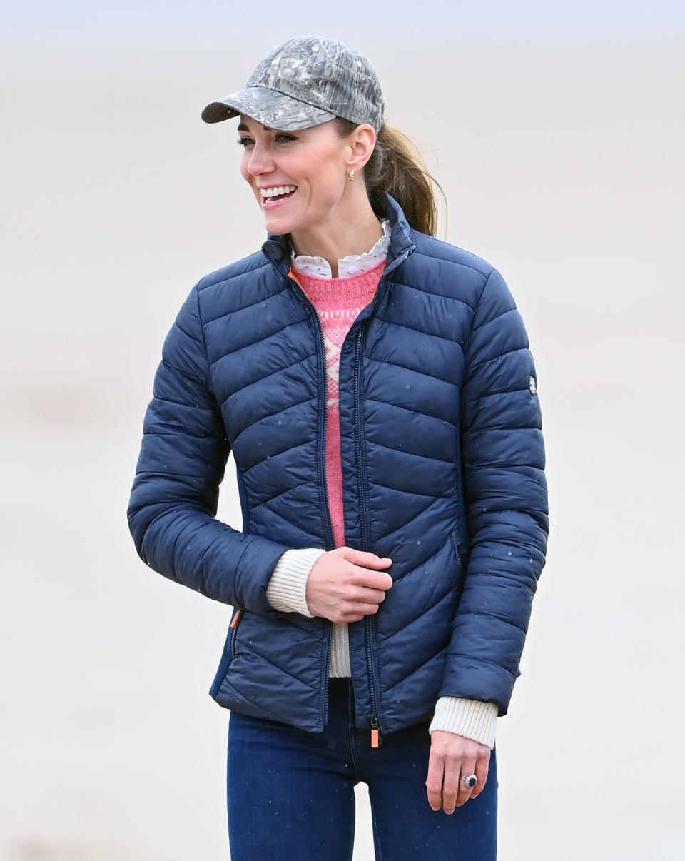 kate middleton in baseball cap and blue quilted barbour jacket, blue jeans, and pink sweater