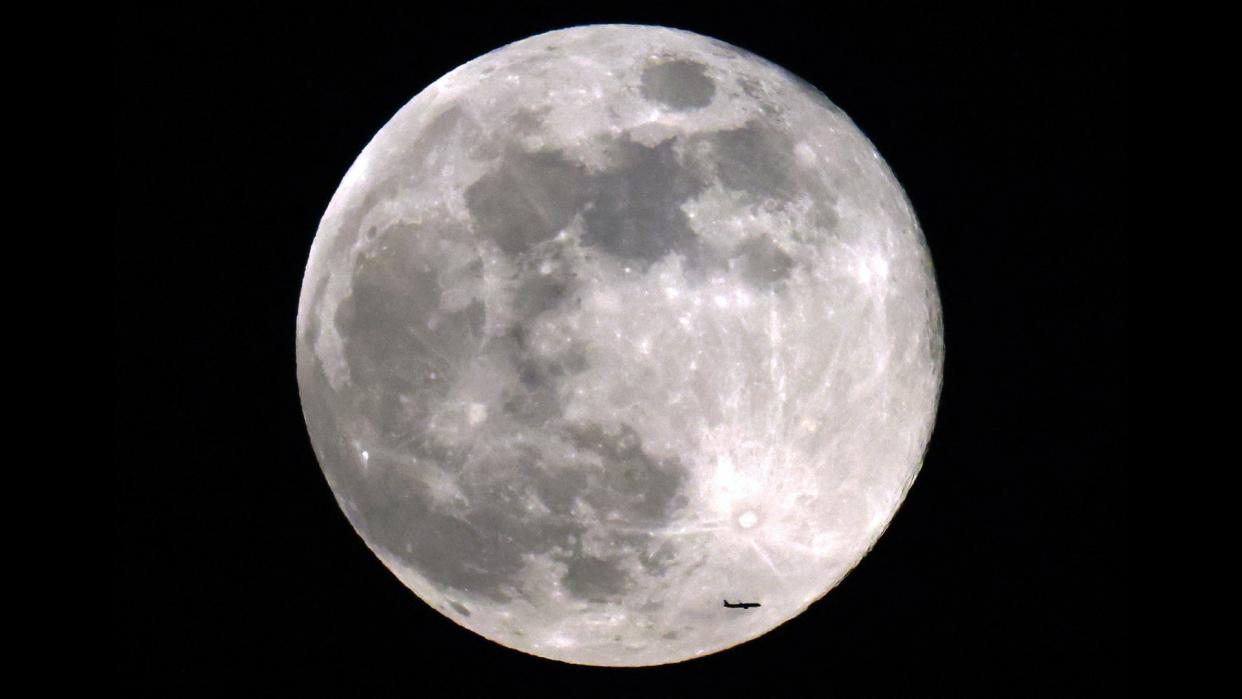  An airplane flies in front of the full moon in a dark sky. 